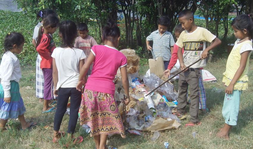 A group of young primary school children use metal tongs to add to their pile of trash