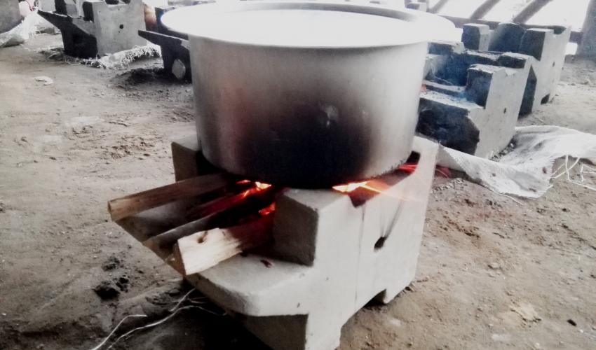 A metal basin heats on top of a small cement cookstove
