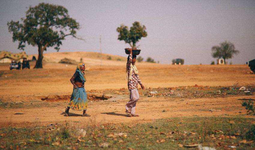 Women walking in dirt with basket on head.