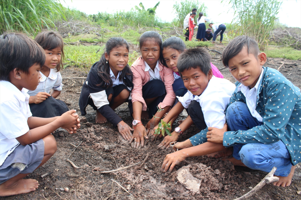 A group of students pose for a picture around a tree seedling they planted