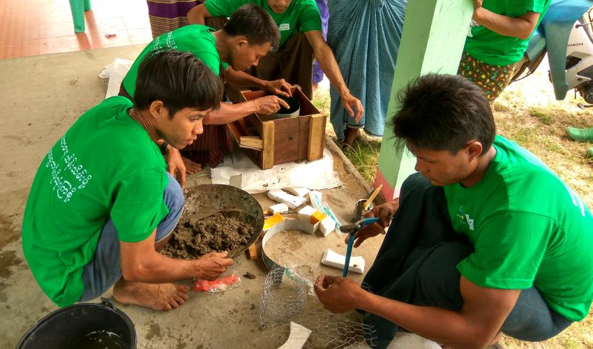 Four men in matching green shirts practice making stoves step by step