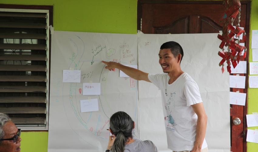 A man in a white shirt points to a map drawn on a large piece of paper
