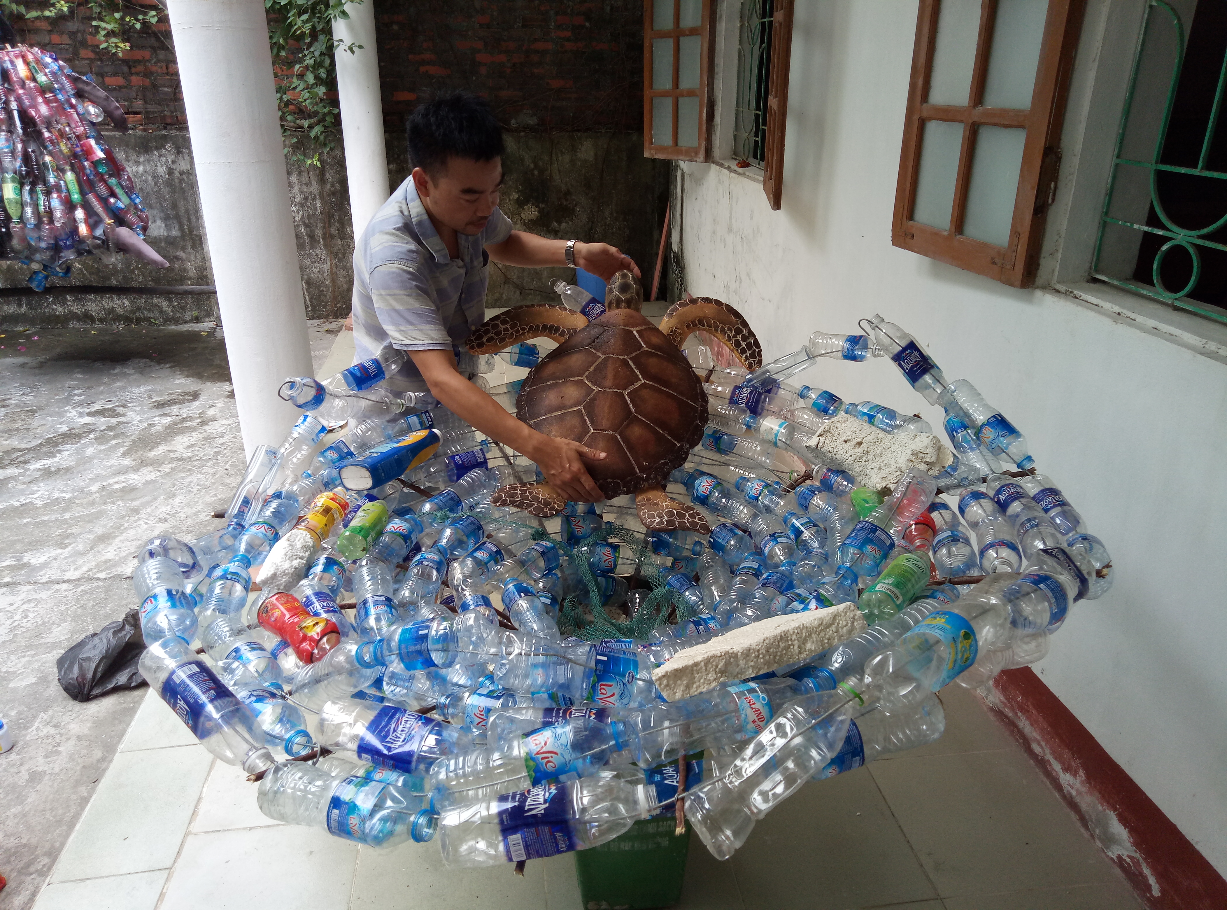 “Help” shows a sea turtle stuck in a cyclone of plastic bottles by Dau Quyet Tien made from foam and plastic bottles 