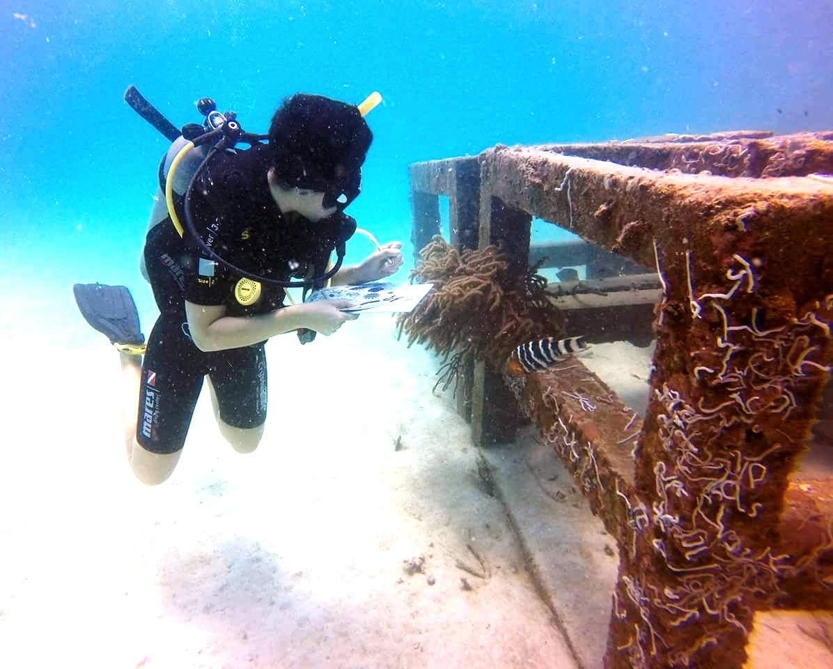 A diver takes notes on reef fish swimming near marine debris