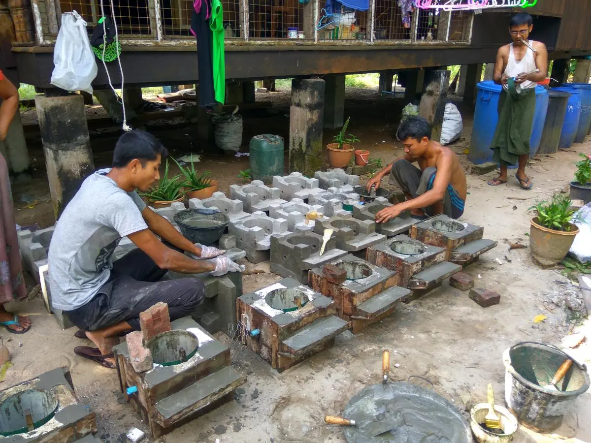 Two men crouch on the ground making cement cookstoves