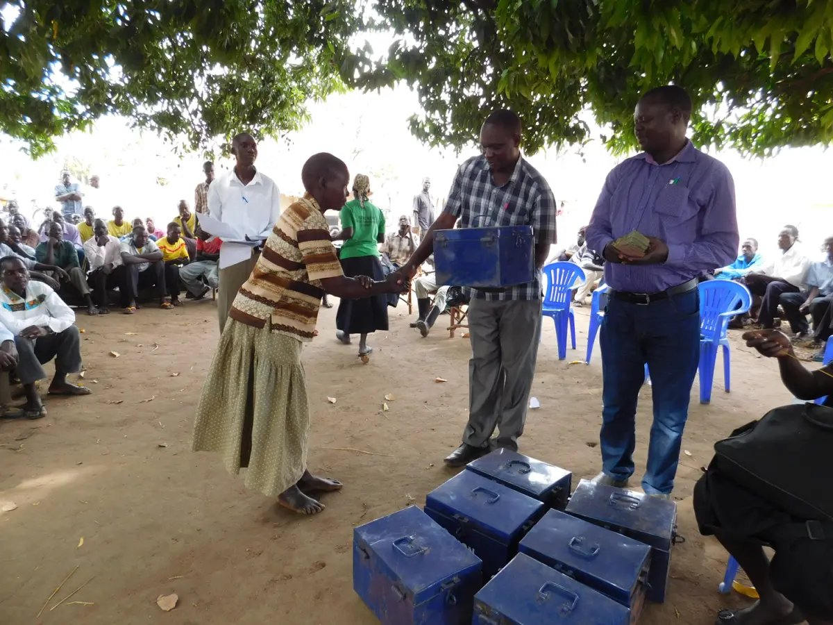 two men handing blue box to woman. shaking hands